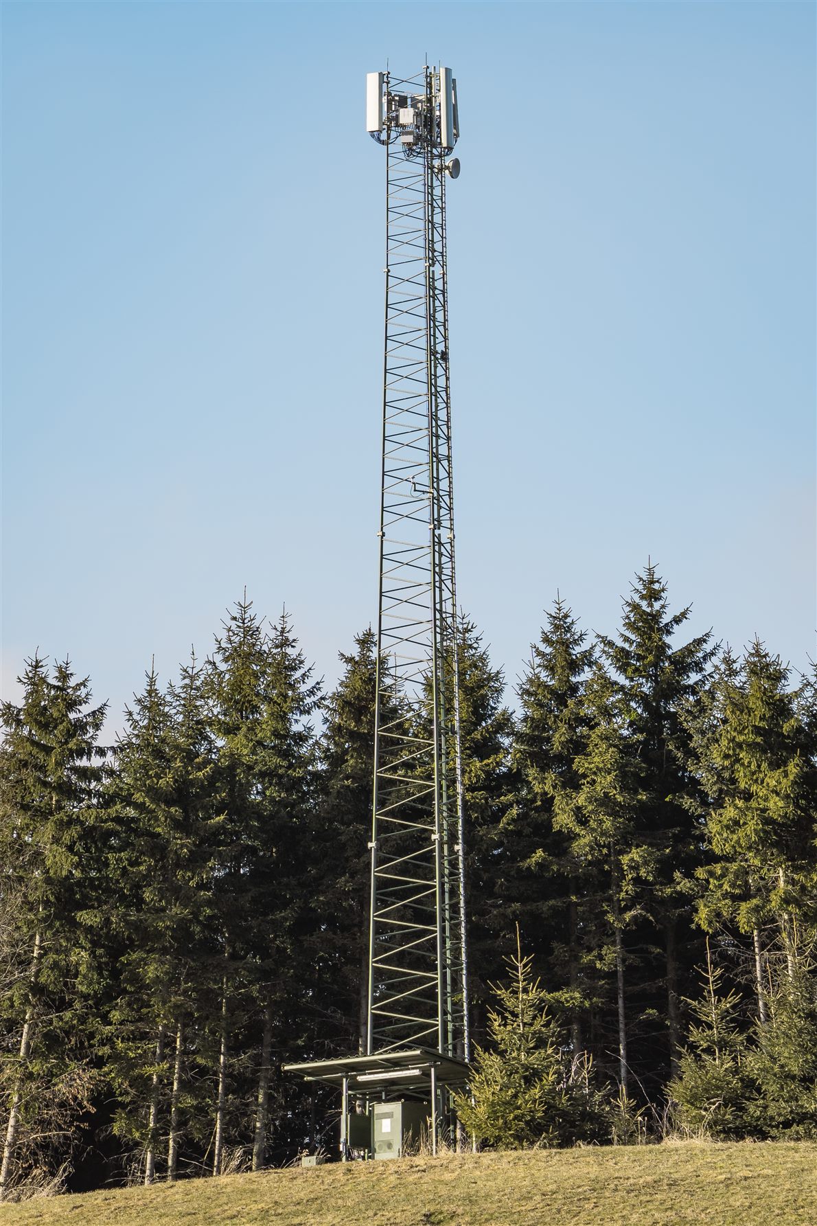 Lattice mobile base station mast against a forest and blue sky