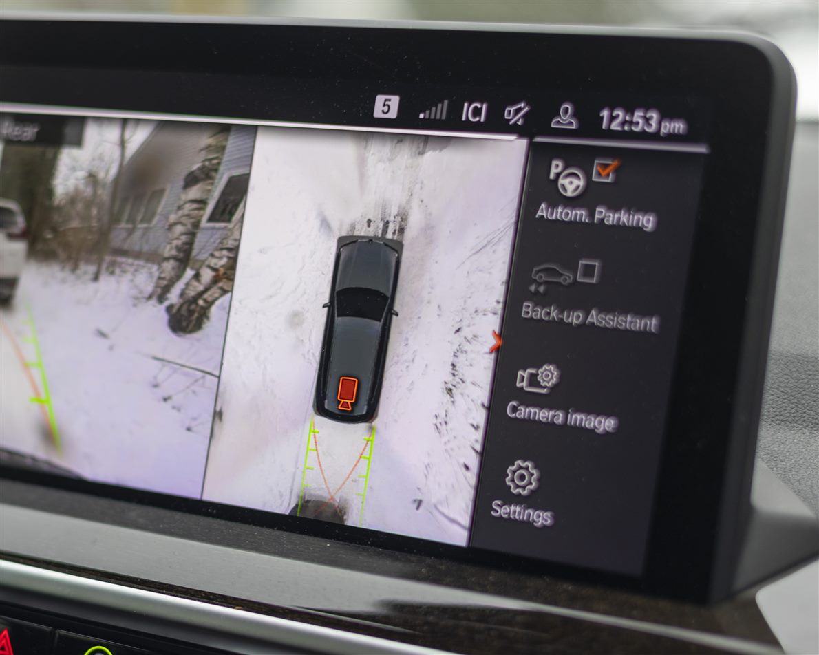 Infotainment screen showing a stitched top-down surround view of a parked car on snowy ground beside a rear camera view