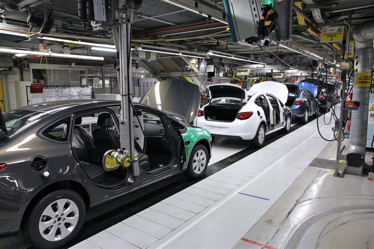 Car bodies moving along a factory assembly line with overhead carriers and marked floor lanes