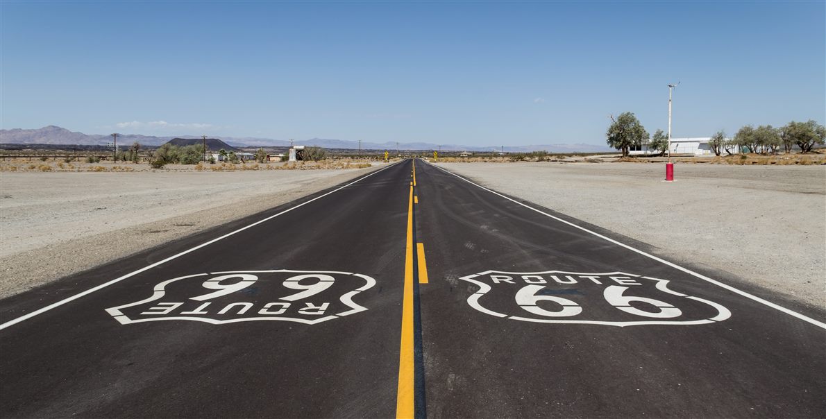 Straight desert highway with a yellow center line, white edge lines and Route 66 markings painted on the asphalt
