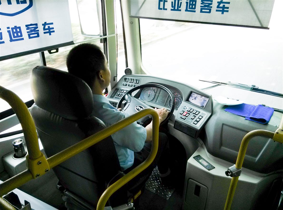 Bus driver at the wheel with a small dashboard display screen beside the instrument cluster