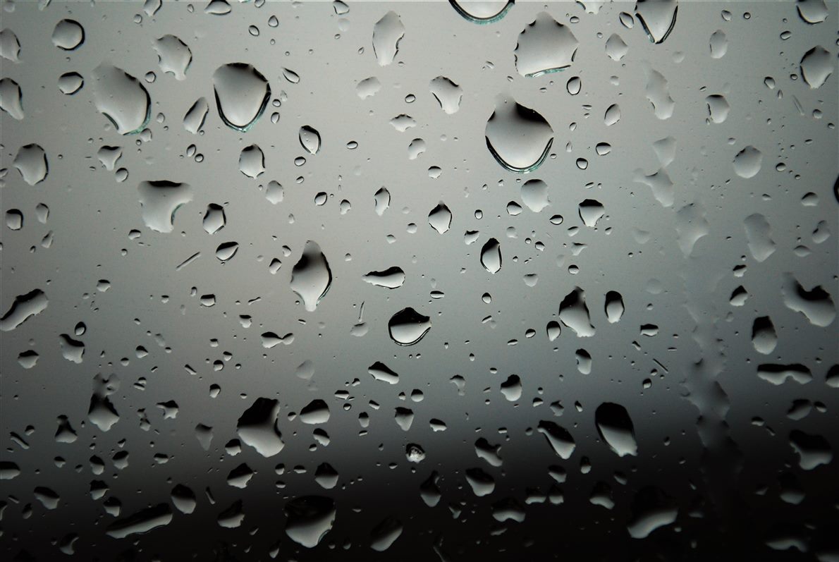 Close view of water droplets clinging to a glass surface, the scene behind them blurred and broken into fragments
