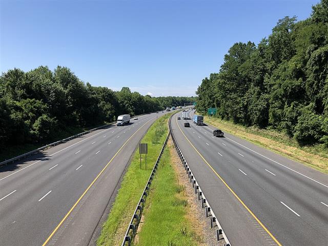 A divided highway seen from an overpass, white dashed lane lines and yellow edge lines marked along both carriageways on open asphalt