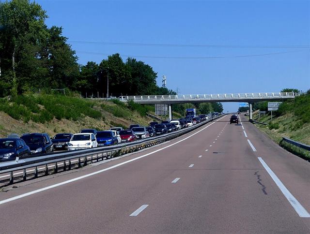 A multi-lane motorway with one carriageway queued bumper to bumper with closely following cars, the opposite lanes running clear