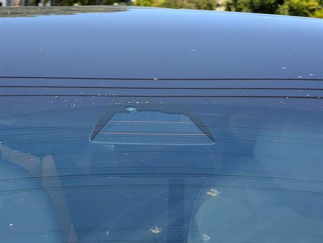 The trapezoidal housing of a forward-facing driver-assistance camera seen through a car's tinted windscreen