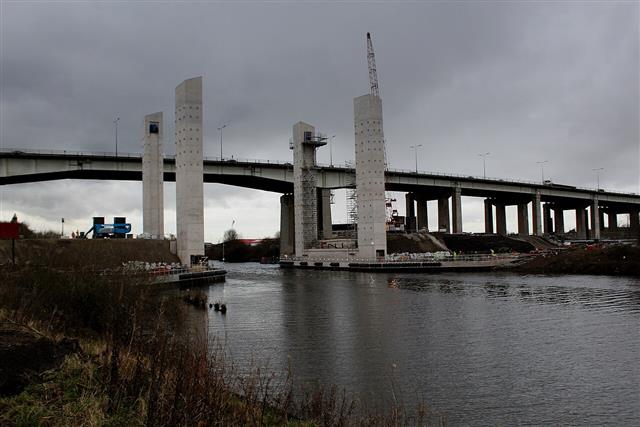 A long road viaduct carried on tall concrete piers above a river, seen from the side